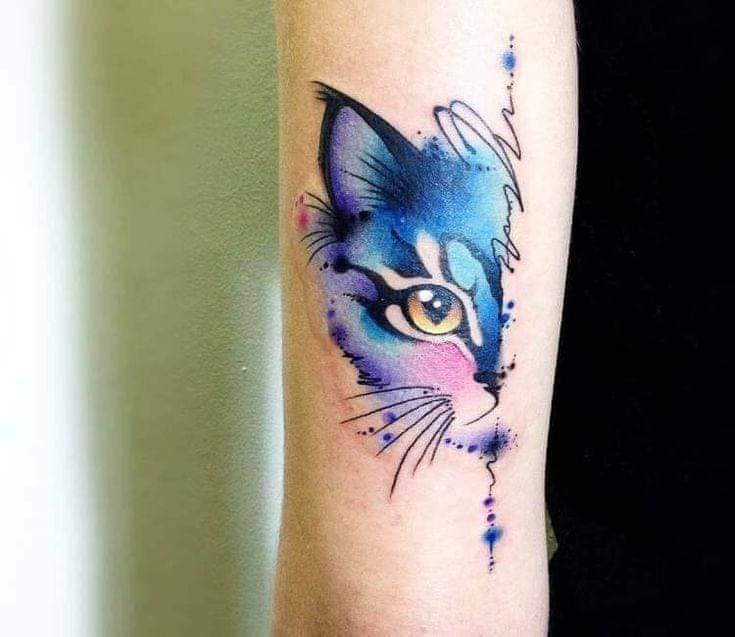 Tatuajes de Gatos Mitad de cara de gato dividida por inscripcion tonos celestes y violaceos acuarela en brazo