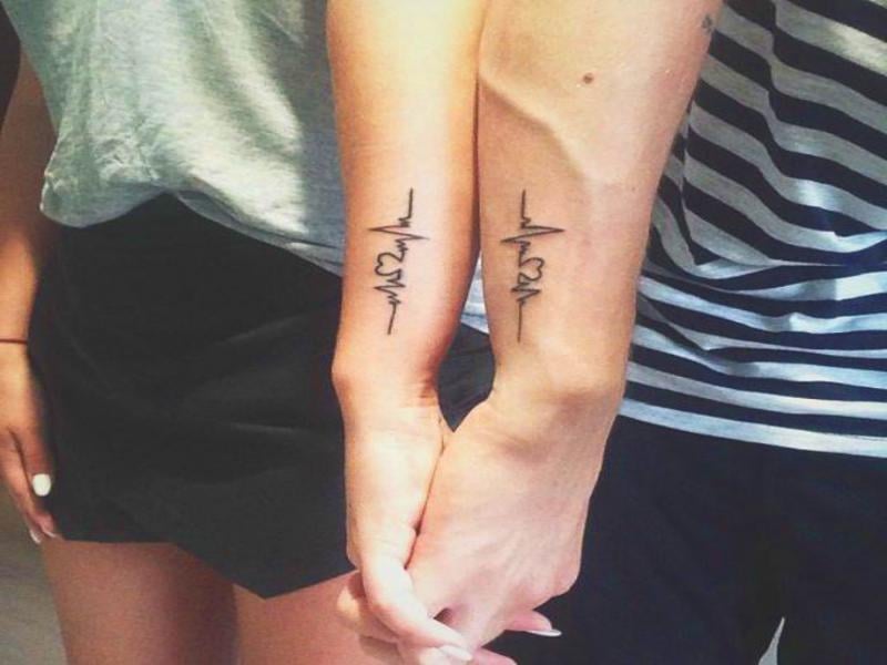 Kleine und komplementäre Tattoos für Paare an den Handgelenken. Elektrokardiogramm mit Herz
