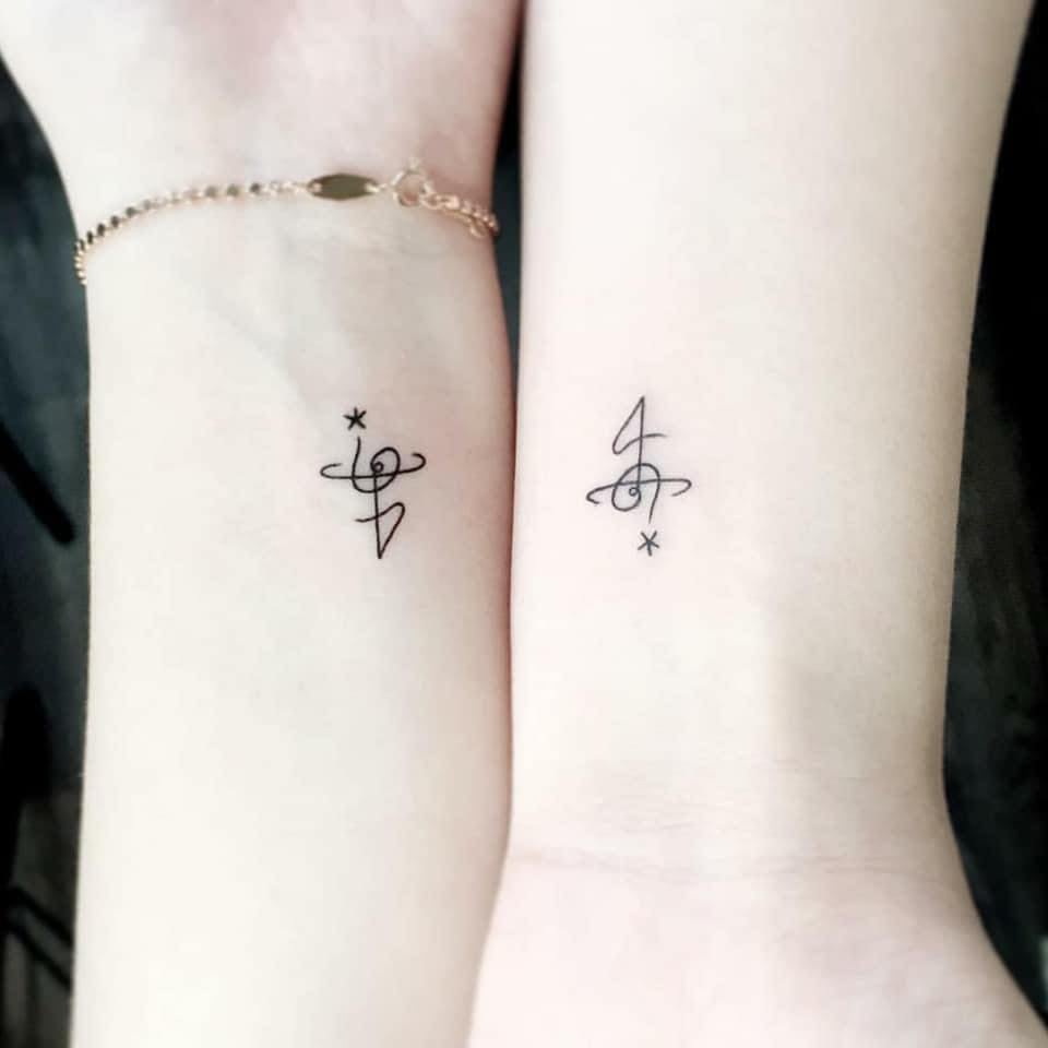 Kleine und ergänzende Tattoos für Paare auf den Handgelenken mit Symbolen, die einer Musiknote mit Stern oder dem Buchstaben Jota ähneln