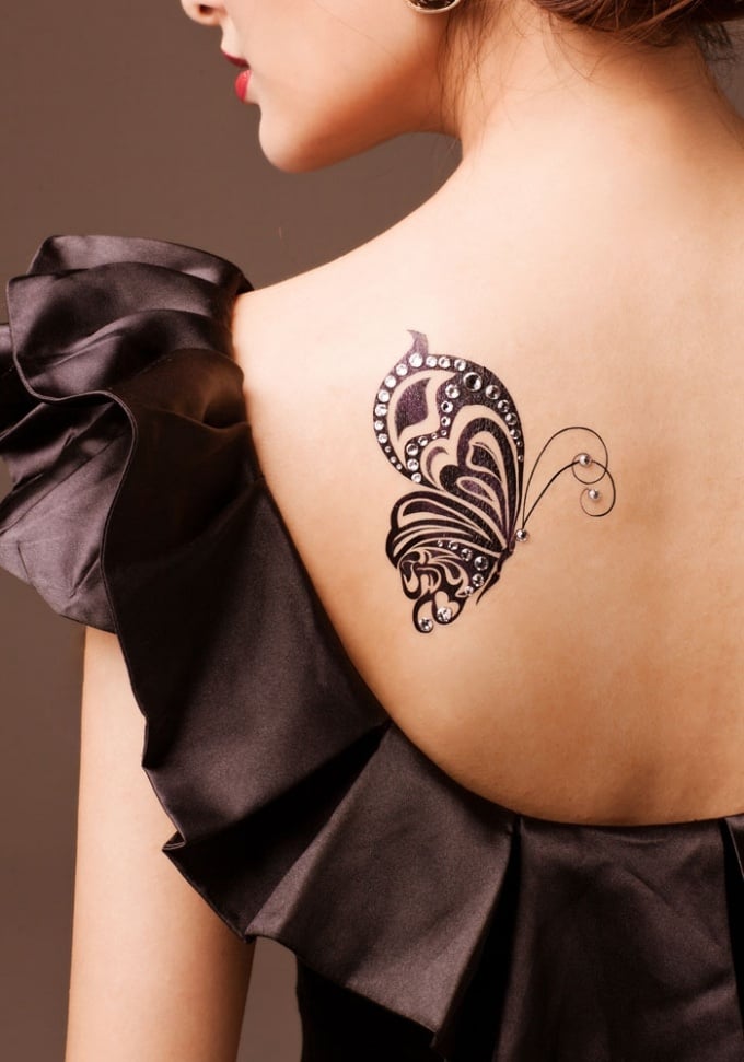 17 Tattoos auf dem Rücken einer Frau, ein halber schwarzer Schmetterling auf dem Schulterblatt mit brillanten Verzierungen