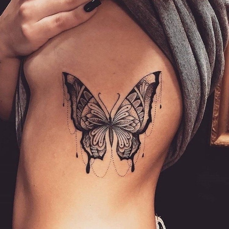 Tatouage de grand papillon noir avec des motifs et des chaînes suspendues sur le côté des côtes de la poitrine d'une femme