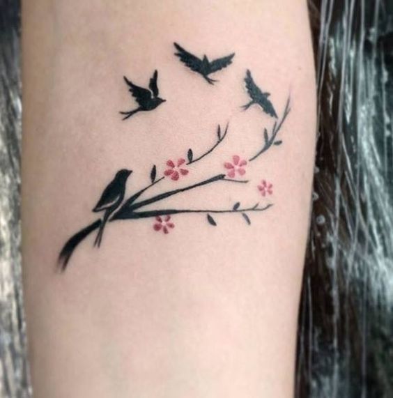 3 TOP 3 Tatuagens de Pássaros e Cores Quatro pássaros pretos um empoleirado no galho com pequenas flores rosa Braço