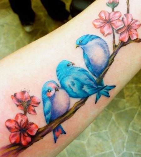 4 TOP 4 Tattoos mit Vögeln und Farben Bunte himmelblaue Vögel sitzen auf einem Pfirsichzweig mit rosa Blumen auf dem Unterarm