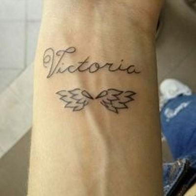 Tätowierungen mit Namensflügeln eines Engels am Handgelenk mit dem Namen Victoria