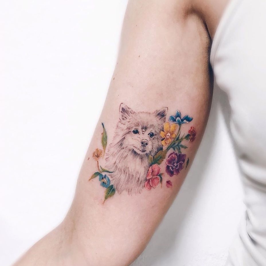 Tatuajes de perros con ramito de flores de varios colores en brazo azul naranja violeta