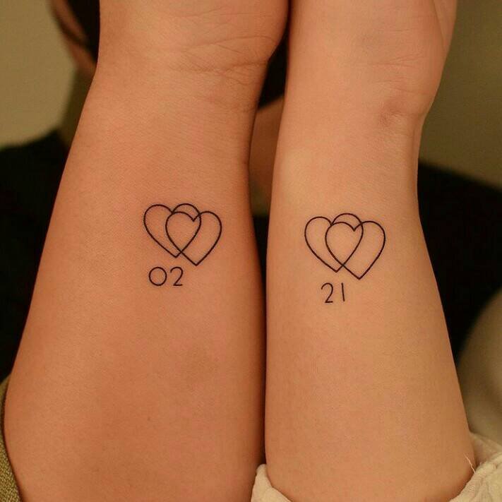15 Small Minimalist Tattoos Paired double heart overlaid with numbers 02 and 21 on wrists