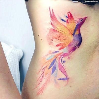 19 Tatuaje de Ave Fenix trazo definido en colores vivos al costado del abdomen naranja violeta fucsia bordo