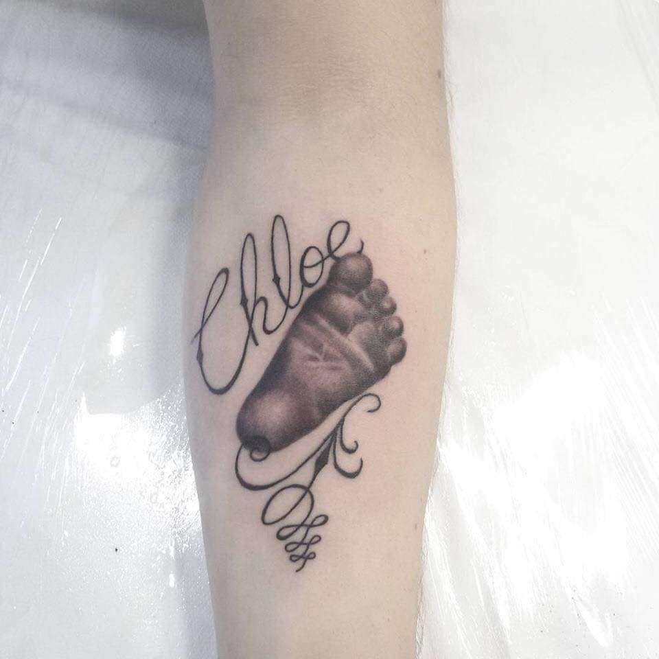 69 Babyfüße-Tattoos auf dem Unterarm mit dem Namen Chloe und Ornamenten in Schwarz