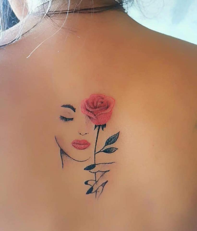 I tatuaggi femminili più apprezzati delineano perfettamente il contorno del volto di una donna che tiene una rosa sulle labbra rosse della schiena