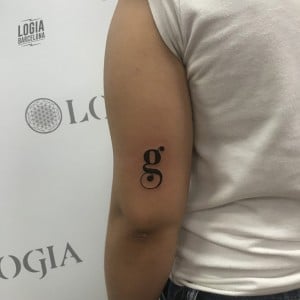 Tatuajes con la letra G ge cerca del codo en negro