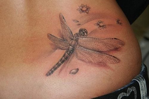 Tatuagens de libélula na cor cinza-marrom com algumas flores na lateral do abdome inferior