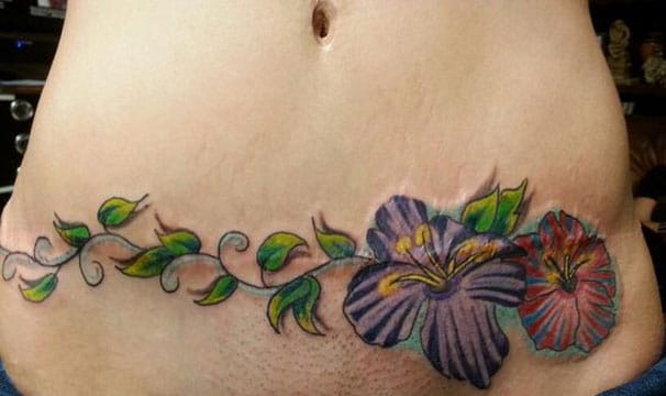Tatuajes para tapar cesarea horizontal ramas verdes y flores azules y rojas de enredadera