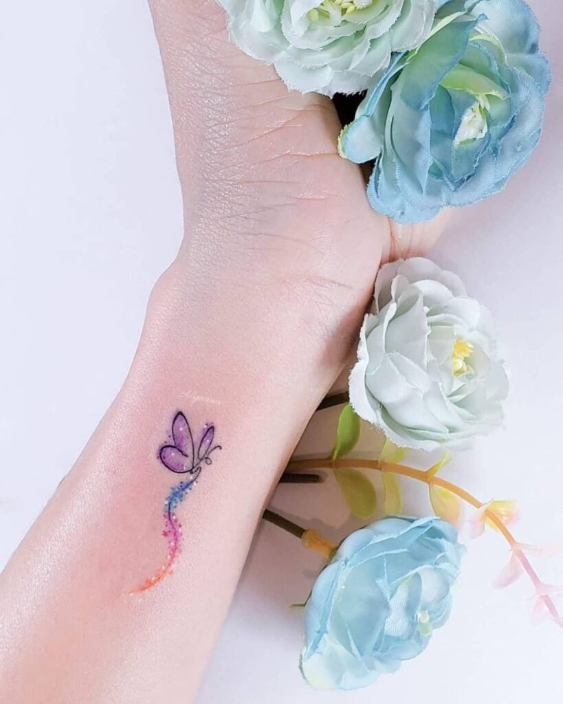 10 Estudio Alynana Tattoo CDMX zarter violetter Schmetterling mit Farbspur und Sternen am Handgelenk