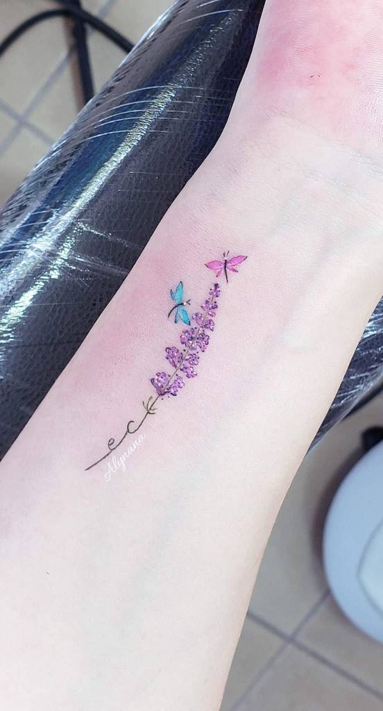 21 Estudio Alynana Tattoo CDMX Raminho de lavanda com iniciais e duas libélulas, uma azul claro e outra rosa representando as crianças no pulso