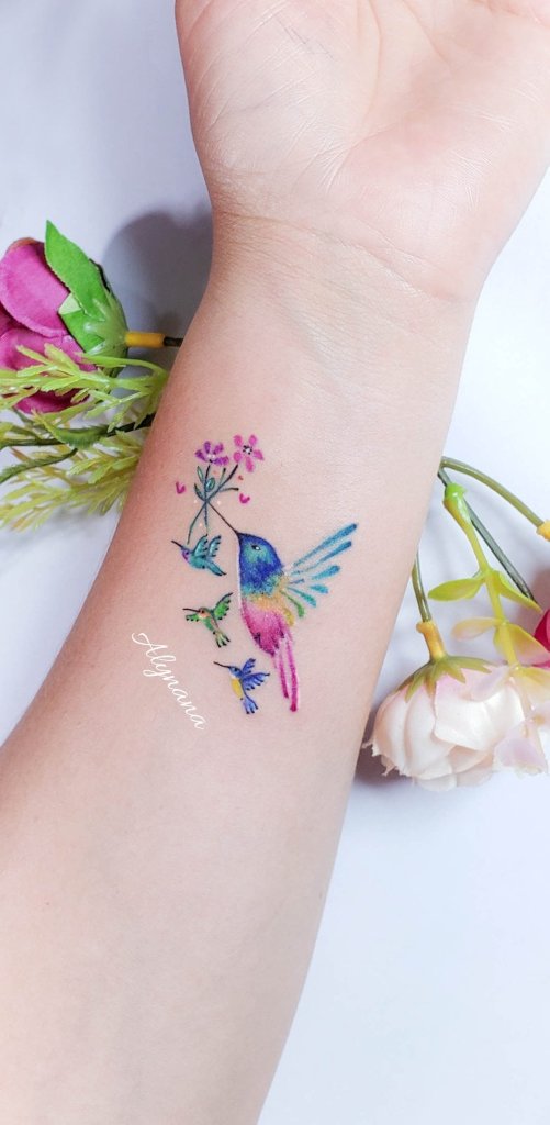 7 Estudio Alynana Tattoo CDMX Hummingbird with Three Children biting a bouquet of pink flowers on the wrist