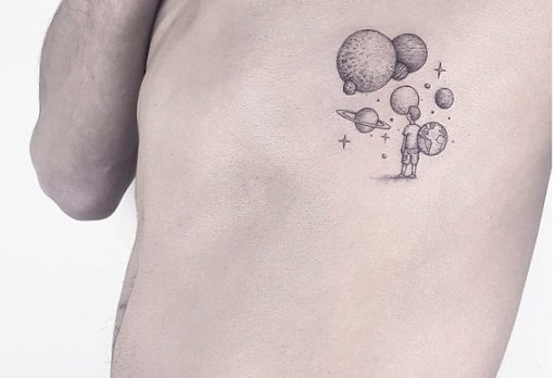 Ragazzo semplice e carino con tatuaggi estetici che guarda i pianeti, alcuni con lune, la terra e le stelle sulle costole