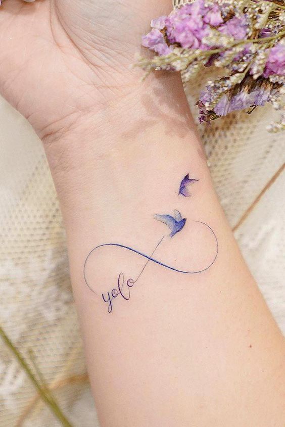 Tattoos der unendlichen Liebe. Zarte Ästhetik, zwei violett-blaue Vögel am Handgelenk und der Name Yofo