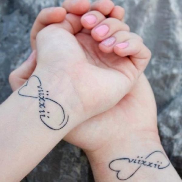 Infinite Love tattoos on two wrists with date of birth in Roman numerals