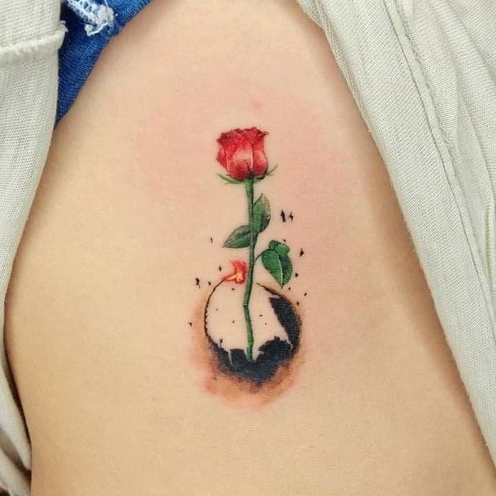Tattoos of Flowers on the Ribs Sapling of a Red Rose with Stem and Green Leaves below Dark Spot that symbolizes the earth
