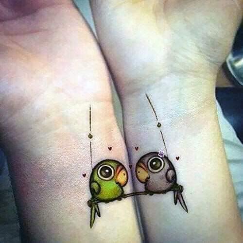 Tattoos für Charakterpaare und mehr Papageien in der Hängematte mit winzigen grauen und grünen Herzen und orangefarbenem Schnabel an den Handgelenken