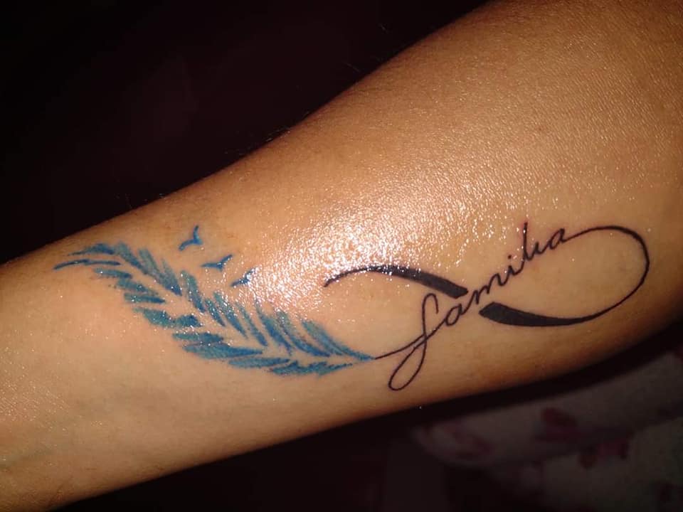 I tatuaggi più apprezzati dalle donne Infinito con la parola Famiglia e una piuma azzurra con tre uccelli