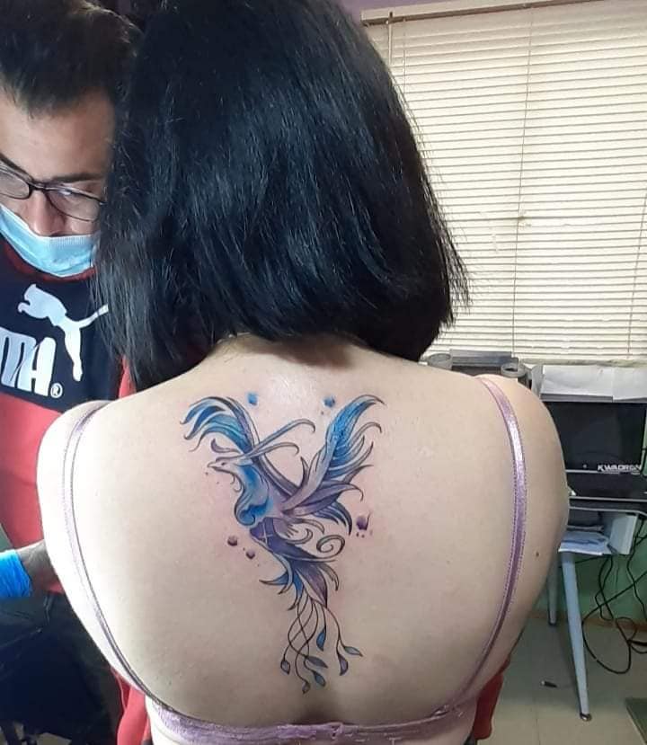 11 Tattoos for women the most liked Ave Fenix in blue and violet tones on the back in the center