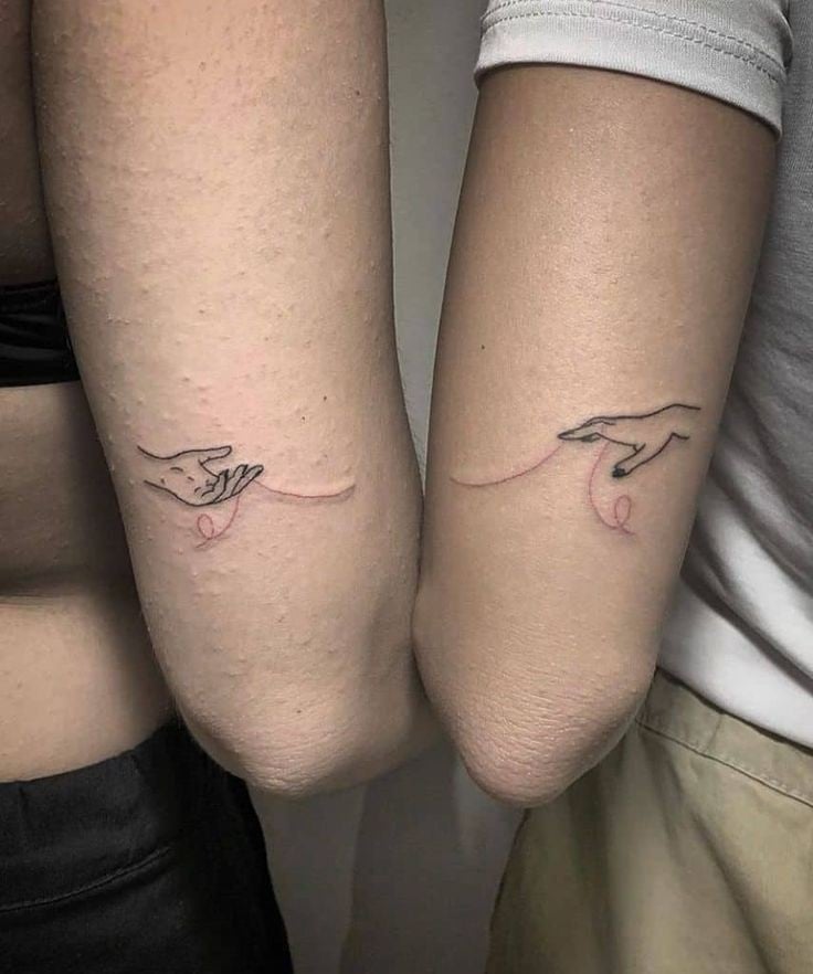 2 Tattoos für beste Freunde auf beiden Armen, Hand mit Handfläche nach oben und Hand mit Handfläche nach unten, die den roten Faden halten, der Schicksale verbindet
