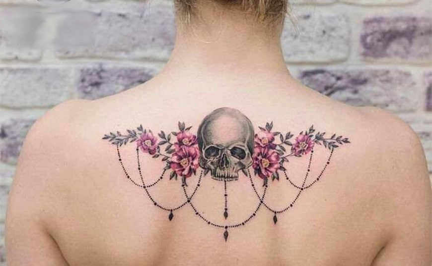 7 Skull tattoos in the middle of the shoulder blades with flower arrangements like angel wings and chain pendants