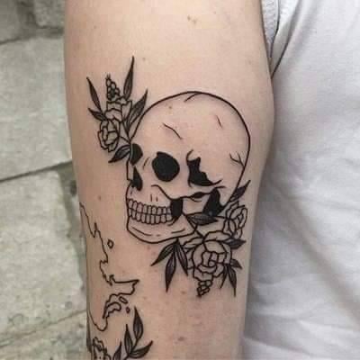 Tatuaggi con teschi in nero. Lavora sul braccio con fiori sui lati