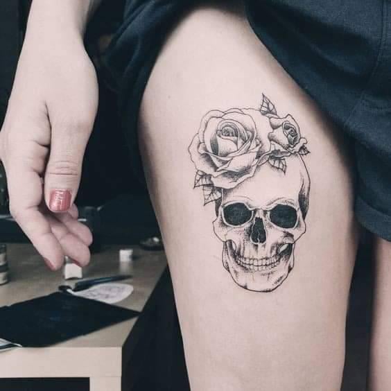 Totenkopf-Tattoos in Schwarz. Auf dem Oberschenkel einer Frau mit Rosen auf dem Kopf