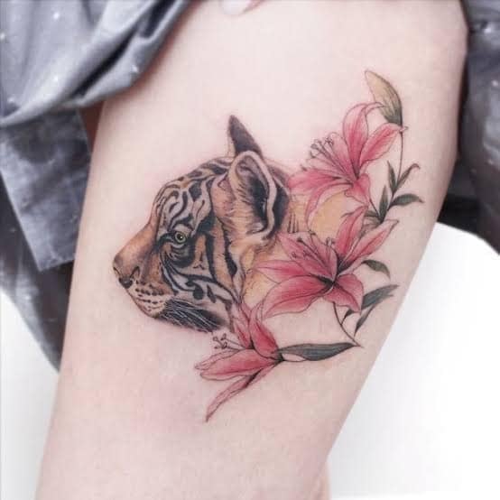 18 süße Tattoo-Ideen. Realistisches Tigergesicht im Profil mit roten Blumen am Oberschenkel