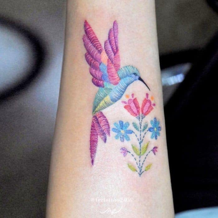 4 TOP 4 Tatuaggi ricamati Artista Fernanda Alvarez Art Mexico Colibrì che morde fiori nei toni viola e azzurro dell'avambraccio