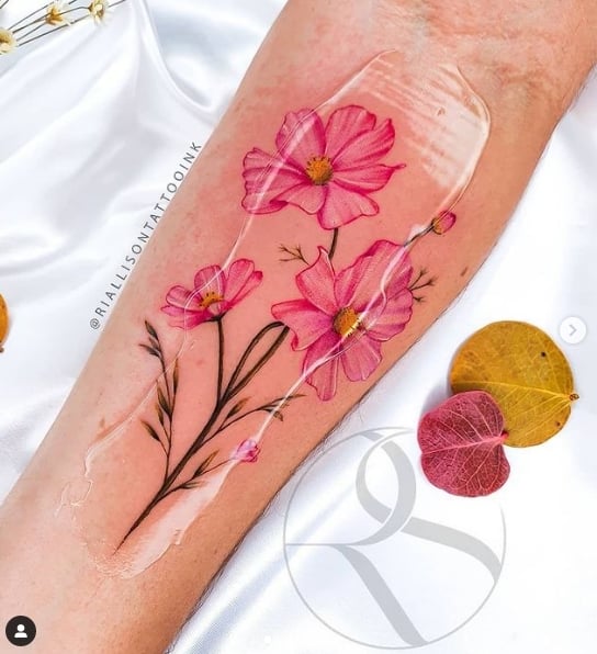 9 fleurs de cosmos rose intense avec des branches sur l'avant-bras Tatoueur Riallison Silva