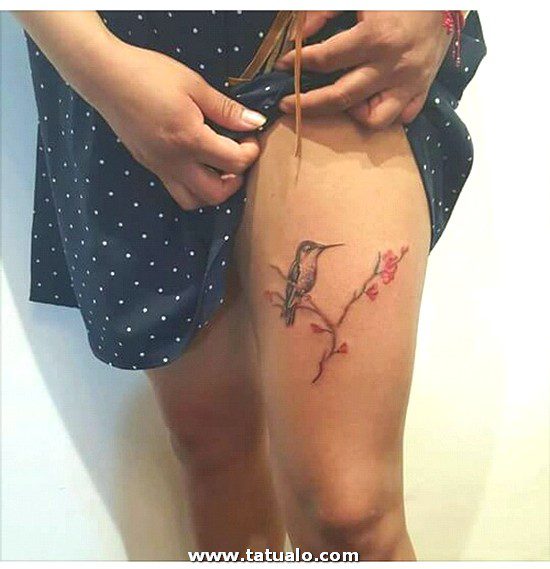 Tatouage sur la cuisse d'une branche de colibri femme et de fleurs rouges