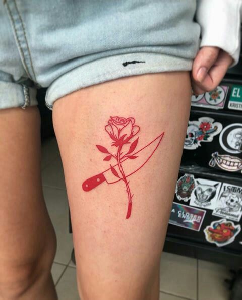 Tattoos mit roter Tinte, Rose und Messer auf dem Oberschenkel einer Frau