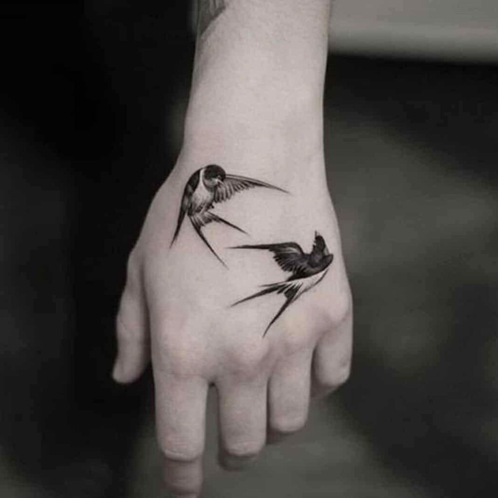 76 Black Tattoo on the Hand Two Swallows fighting or mating on the back
