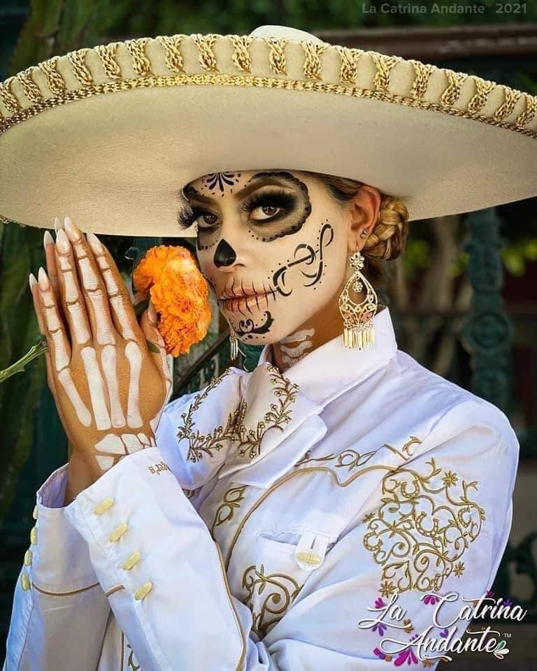 16 La Catrina-Kostüme, einfaches Make-up mit Symbolen im Gesicht, Skelett in den Händen, Anzug und traditioneller Hut mit orangefarbener Blume in der Hand und gesammelten Haaren