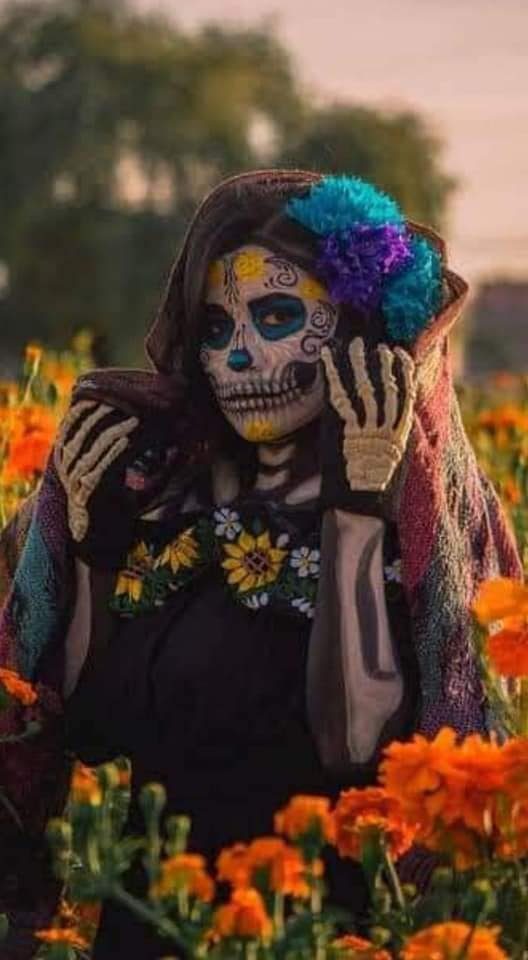 21 La Catrina Costumes maquiagem esqueleto com flor cempasuchil nos olhos detalhes de flores azuis e amarelas cabelo solto com flores azuis na lateral vestido preto com girassóis