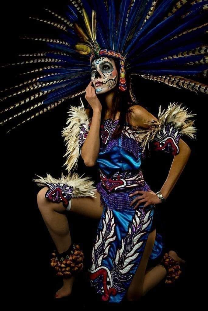 29 Disfraces de La Catrina maquillaje con simbolos en rostro con detalles en azul vestido tradicional indigena en azul con simbolos en blanco diadema de plumas azules largas