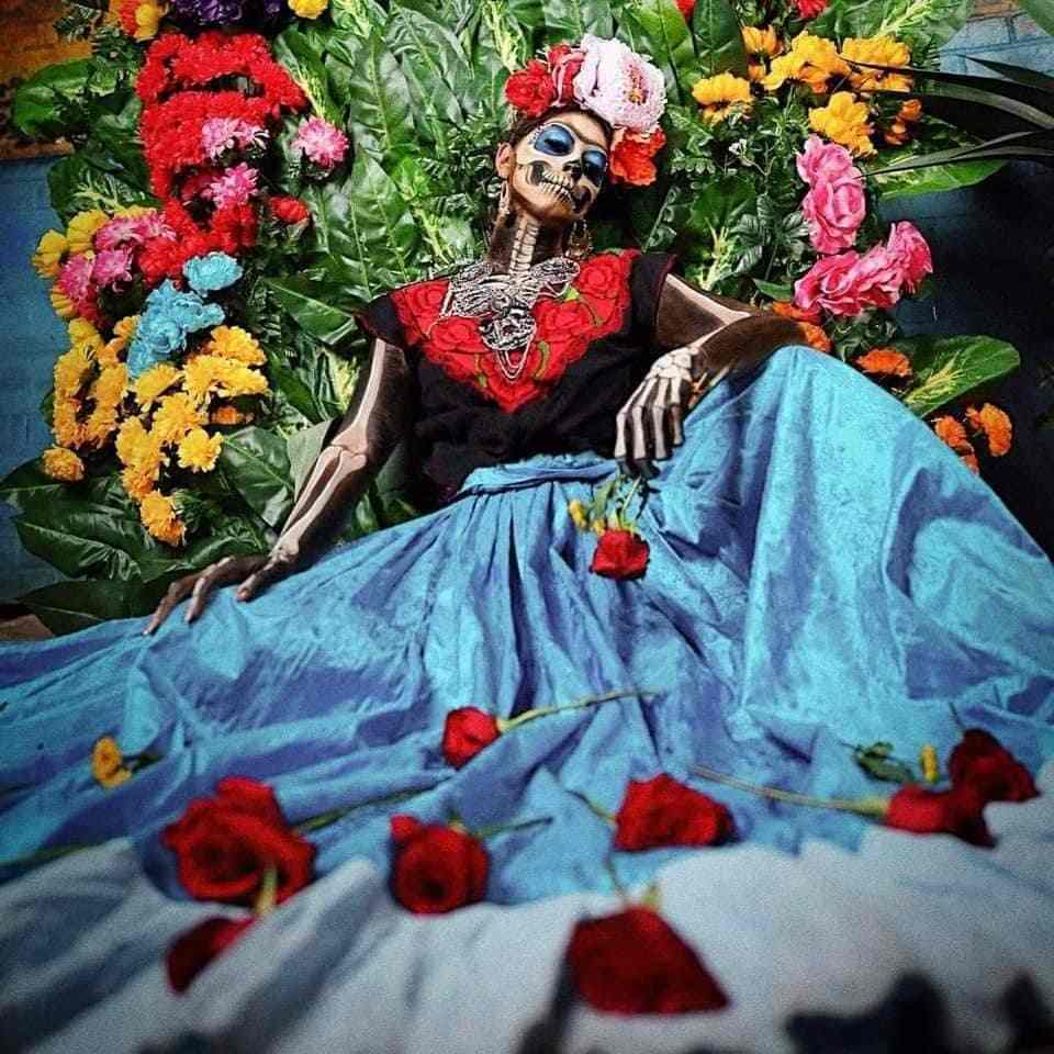 48 La Catrina Kostüme Make-up mit Cempasuchil-Blume in den Augen und Totenkopf im Gesicht und am Körper, Blumenstirnband mit blauem Rock und schwarzer Bluse mit roten Blumen am Ausschnitt