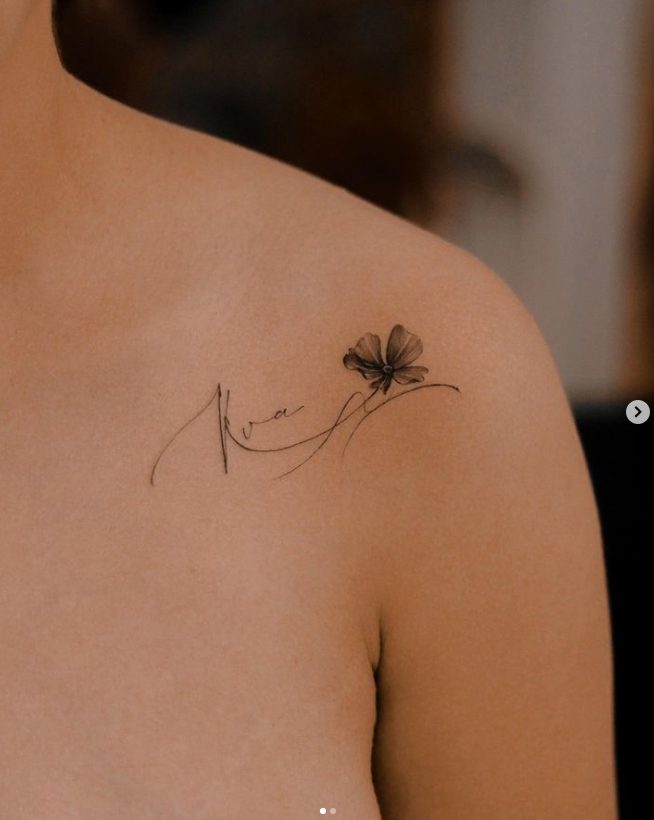38.2 Tattoo by artist Nhi.ink of a delicate flower with letters that look like LOVE on the shoulder