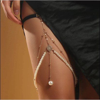 31 Chaînes de jambe de type Body Chains avec sangle noire autour de la jambe et double chaîne fine pendante en forme de V inversé avec sphères dorées et perles blanches