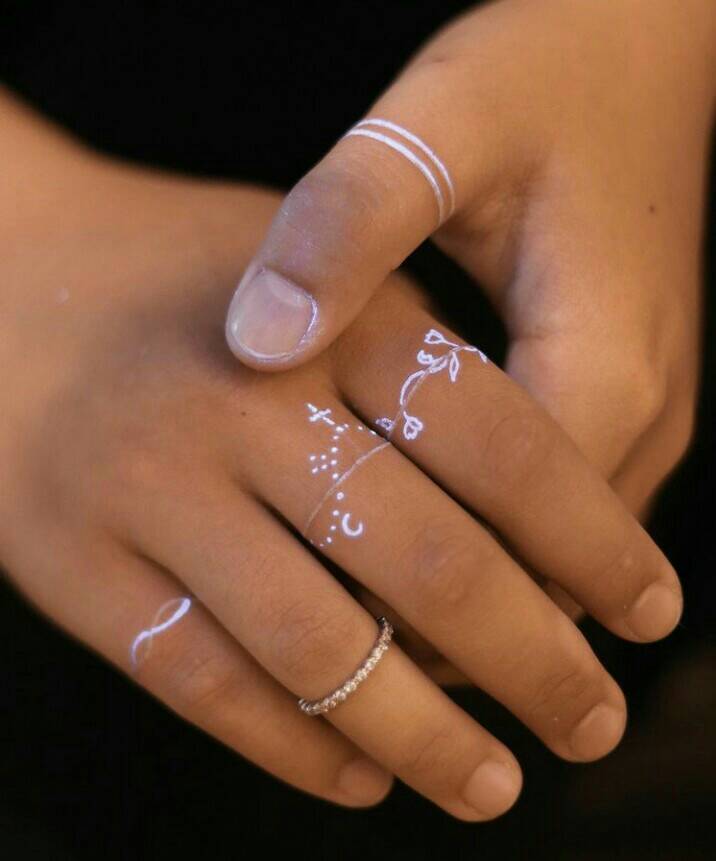 103 Tattoos mit weißem Doppelring am Daumen, Details wie Rosenkranzring und Zweigen an anderen Fingern