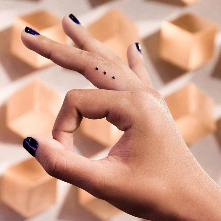 31 tatuagens minimalistas super pequenas de três estrelas nos dedos de uma mulher
