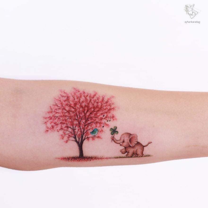Tatoueurs Ayhan Karadağ petit éléphant portant un trèfle sur son tronc et arbre rose aussi petit oiseau bleu