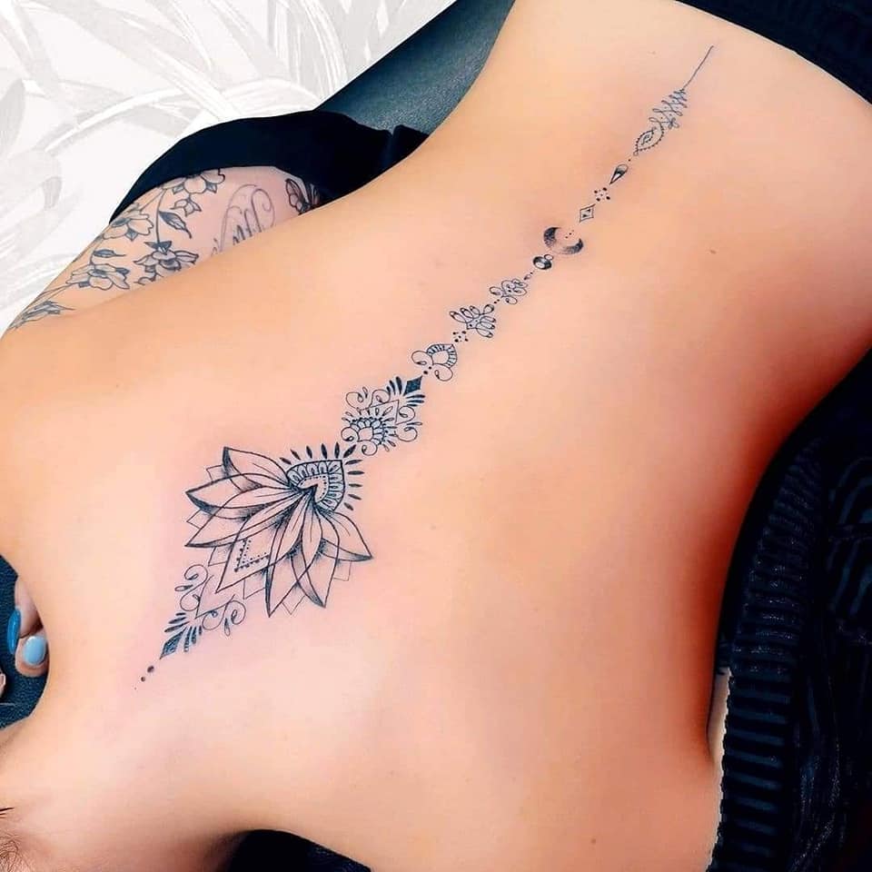 Tatuaggio sulla schiena di una donna lungo la colonna vertebrale, fiore di loto e altre trame
