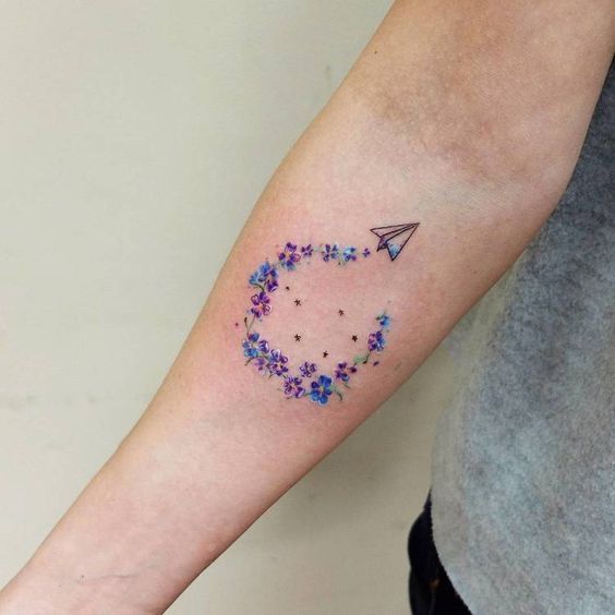 Tatuaje Full Color Pequeno para Mujer avion de papel en antebrazo y estela de estrellas