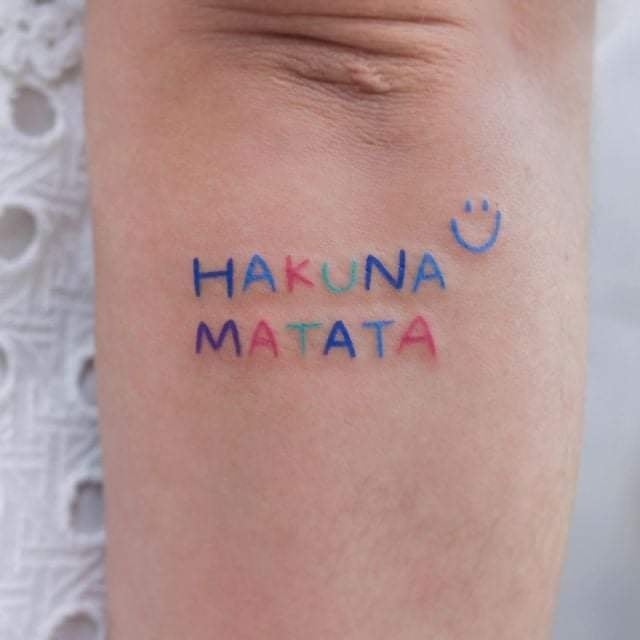 Kleines vollfarbiges Tattoo für Frauen mit Hakuna Matata-Aufschrift und Smile-Gesicht