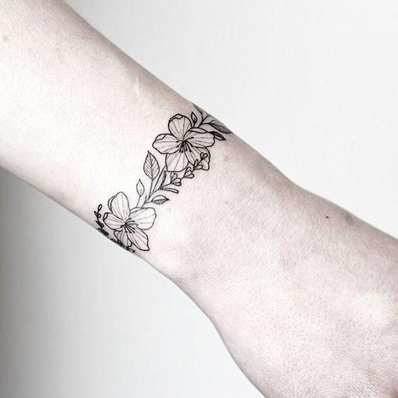 Tattoo mit Armband- oder Armband-Umriss in tiefschwarzen Blumen und Blättern am Handgelenk