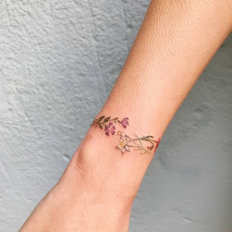 Armband- oder Armband-Tattoo aus Zweigen und rötlichen Blumen am Handgelenk
